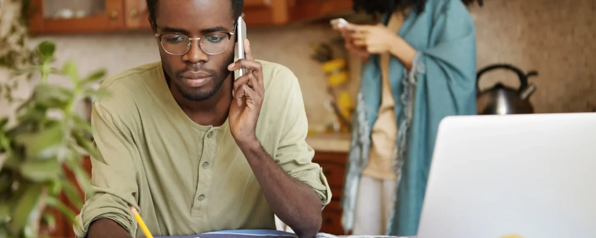 serious-african-man-having-phone-conversation-with-bank-asking-extend-loan-term-paying-out-mortgage-holding-pencil-other-hand-making-notes-documents-lying-table-front-him_compressed